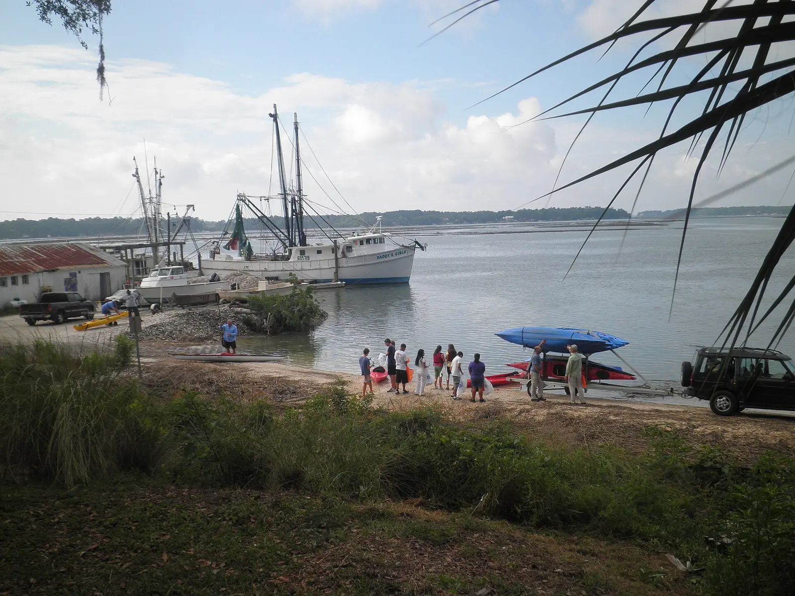 Shrimp boats tie up at the Bluffton Oyster Company dock on the May River as volunteers gather on the shore below Oyster Factory Park.