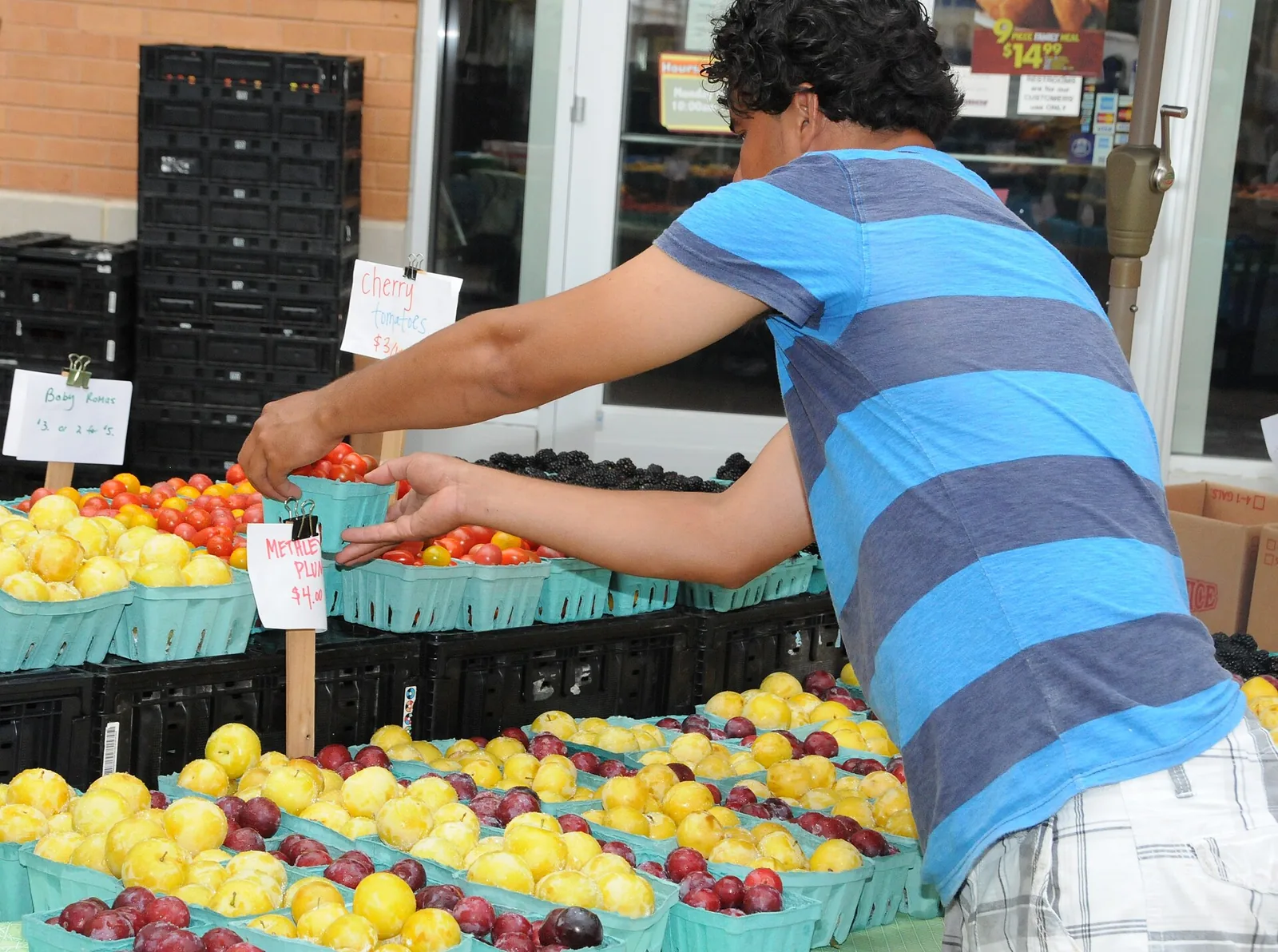 A vendor sets out baskets of cherry tomatoes and plums at a farmers market stand in the Columbia Heights neighborhood of Washington, D.C.
