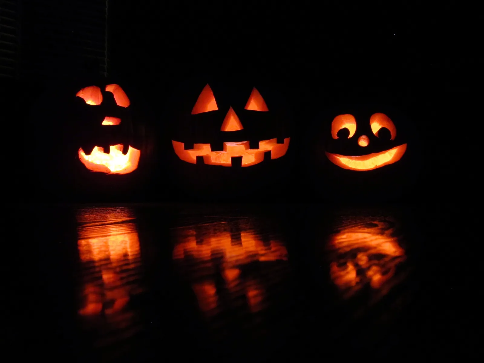 Three carved jack-o'-lanterns glow in the dark on Halloween night.