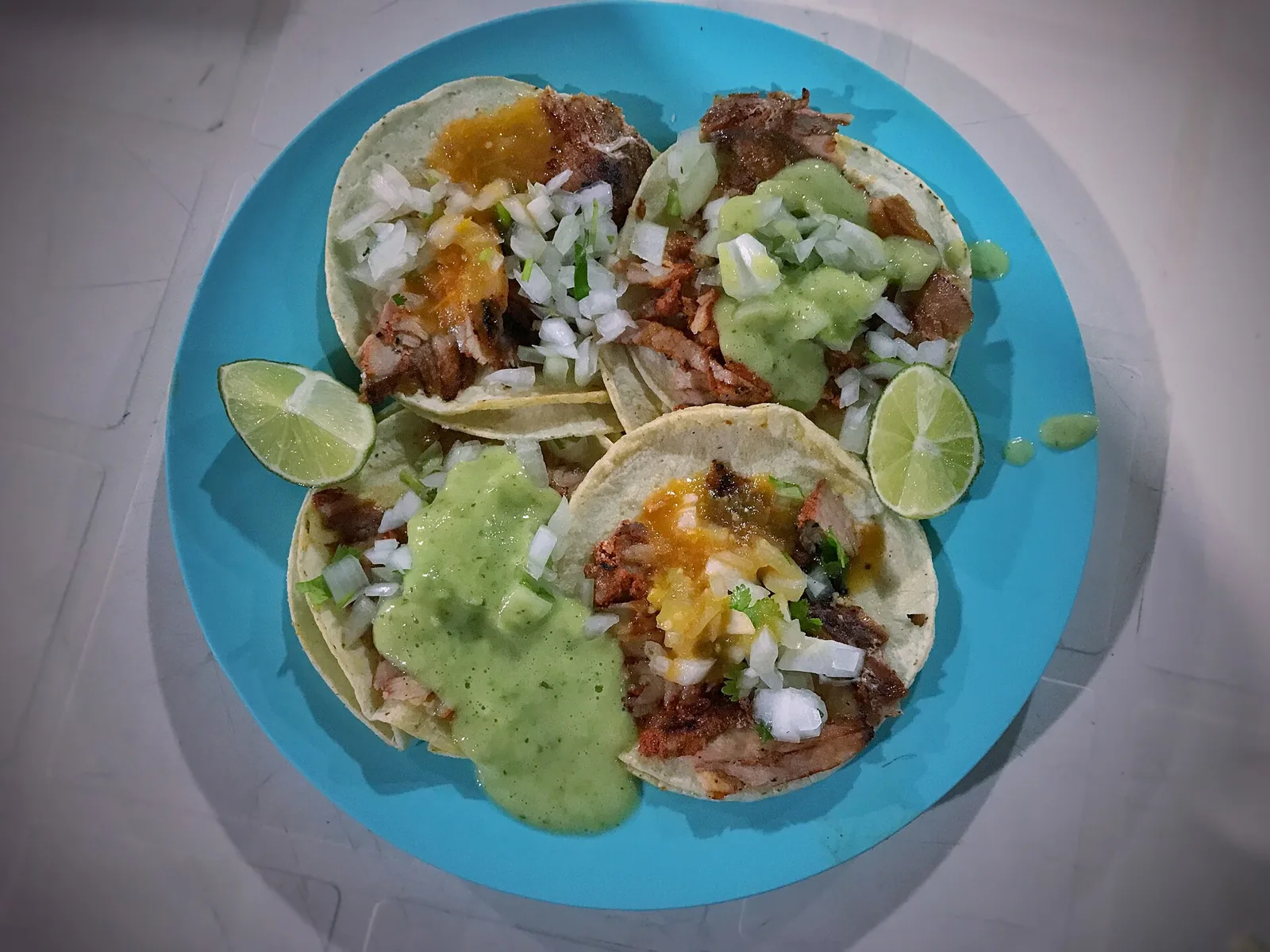 Al pastor tacos with onion, cilantro, salsa and lime on a blue plate at a taco stand in Tulum, Mexico.