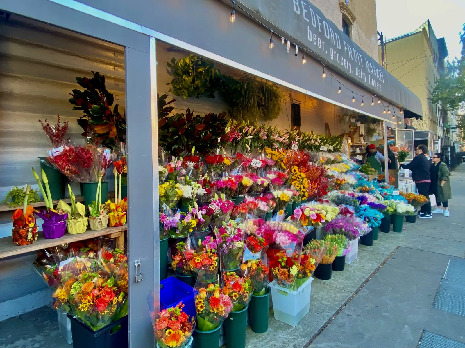 Buckets of cut flowers and bouquets for sale outside a market on a city sidewalk in Brooklyn, N.Y.