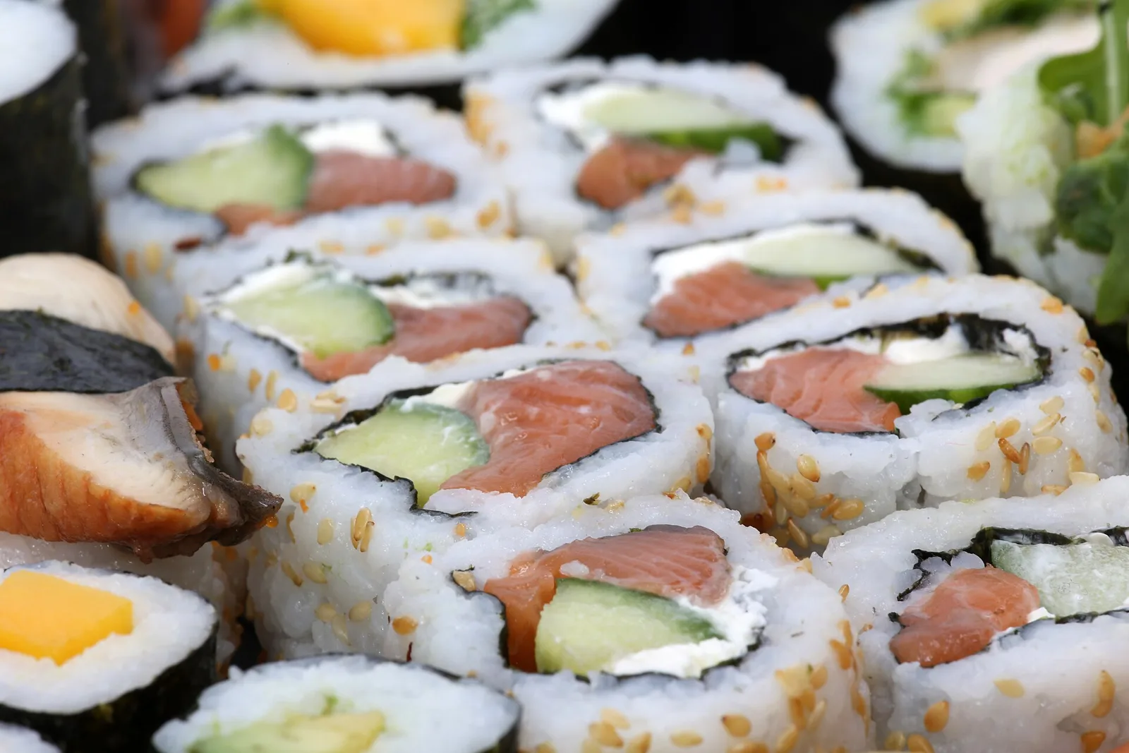 Rows of salmon, cucumber and cream cheese sushi rolls with sesame seeds beside eel and mango pieces. The photo was not taken in Bluffton.