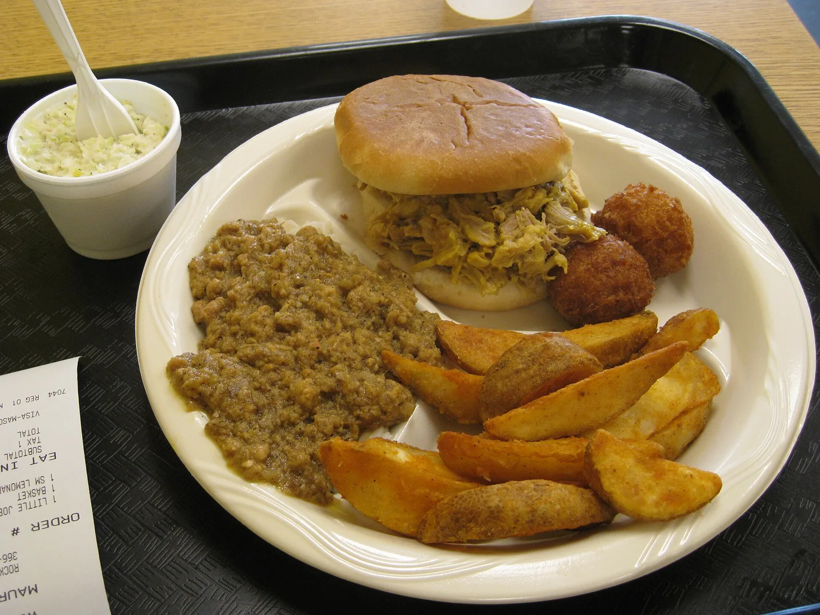 A South Carolina-style barbecue plate with a pulled pork sandwich, hash, hushpuppies, potato wedges and coleslaw at Maurice's Gourmet BBQ. The photo was not taken in Bluffton.