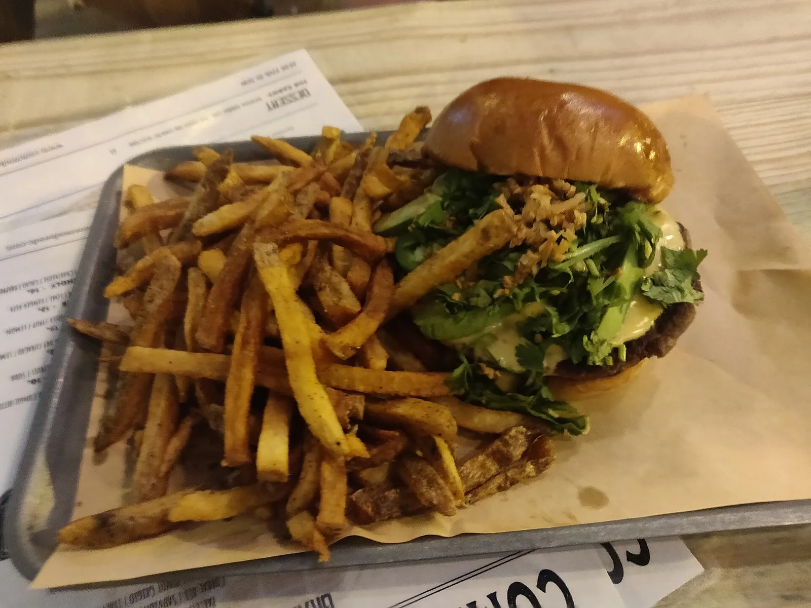 A burger topped with avocado, cilantro and crispy onions next to a pile of fries on a metal tray. The photo was not taken in Bluffton.