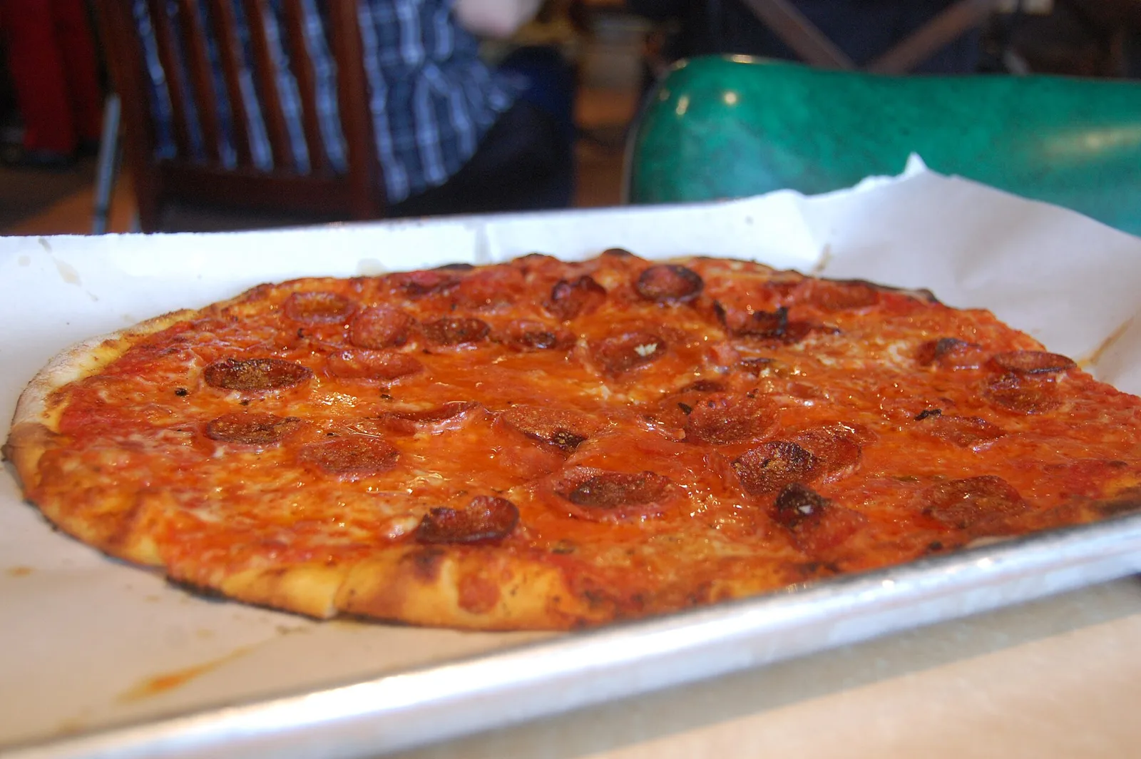 A thin-crust pepperoni pizza on a sheet pan lined with paper. The photo was not taken in Bluffton.