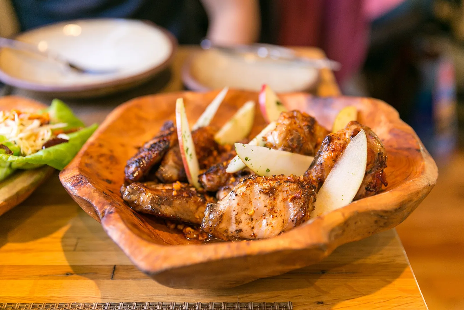 Honey-glazed chicken wings with spiced pecans and apple slices in a wooden bowl. The photo was not taken in Bluffton.